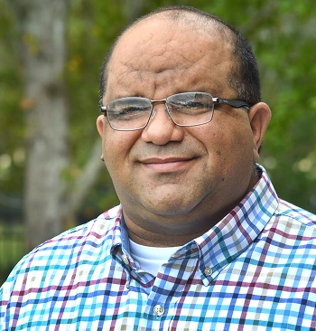 Gustavo Guzman, Licensed Mental Health Counselor, smiling outdoors in a plaid shirt, emphasizing his approachable personality and commitment to mental health support.